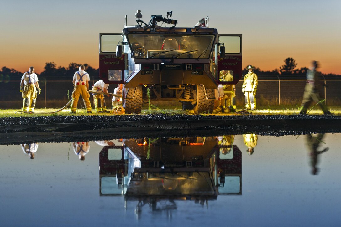 Air Force firefighters put equipment into a truck, as the scene is reflected in water.