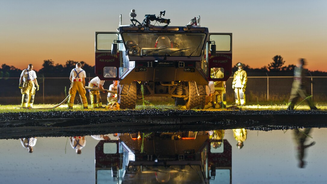 Air Force firefighters put equipment into a truck, as the scene is reflected in water.
