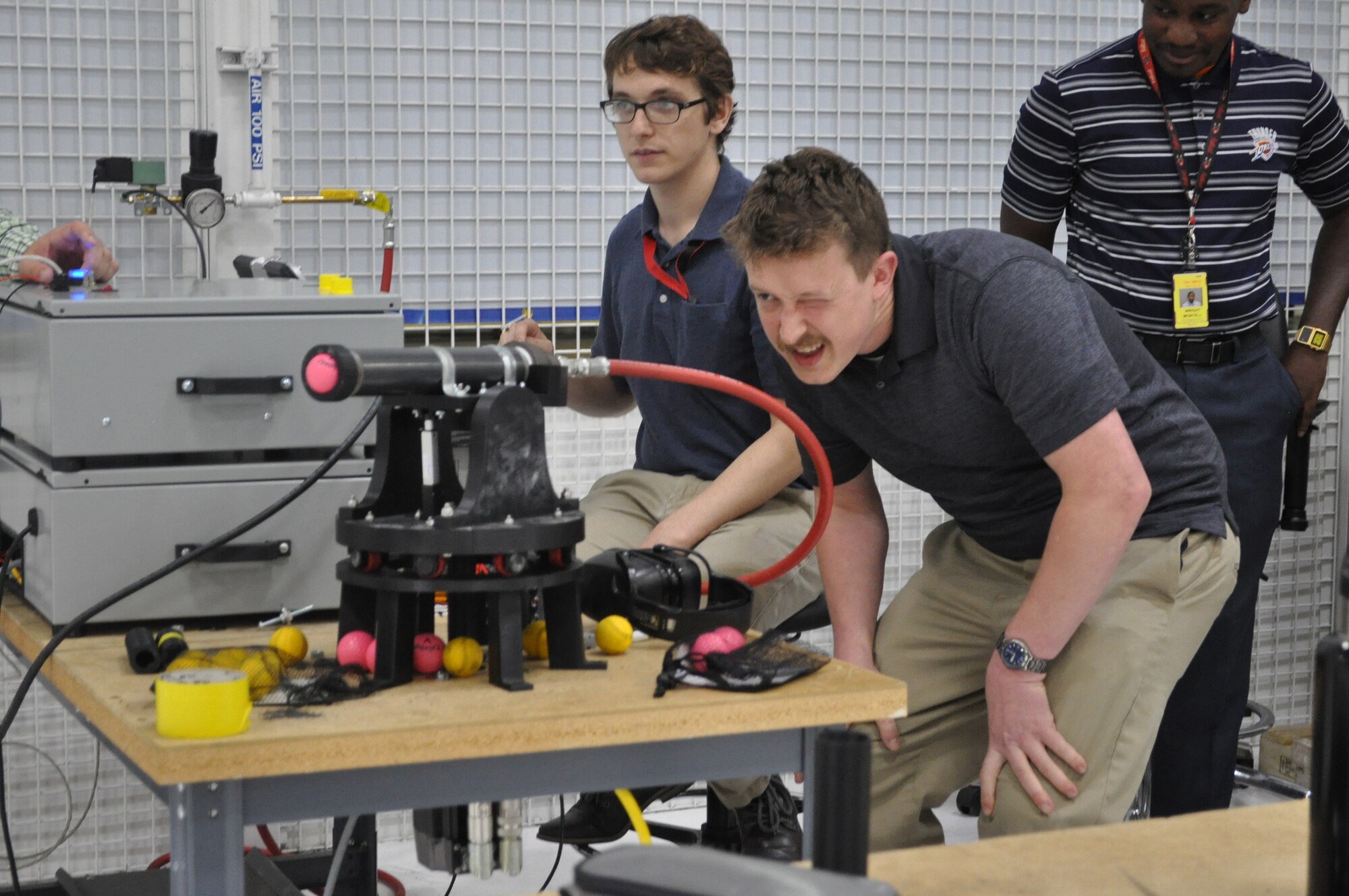 Intern Michael Fleagle eyeballs the trajectory of an air cannon that fires practice golf balls at targets in a competition set up by the 555th Software Maintenance Squadron in Bldg. 9001.