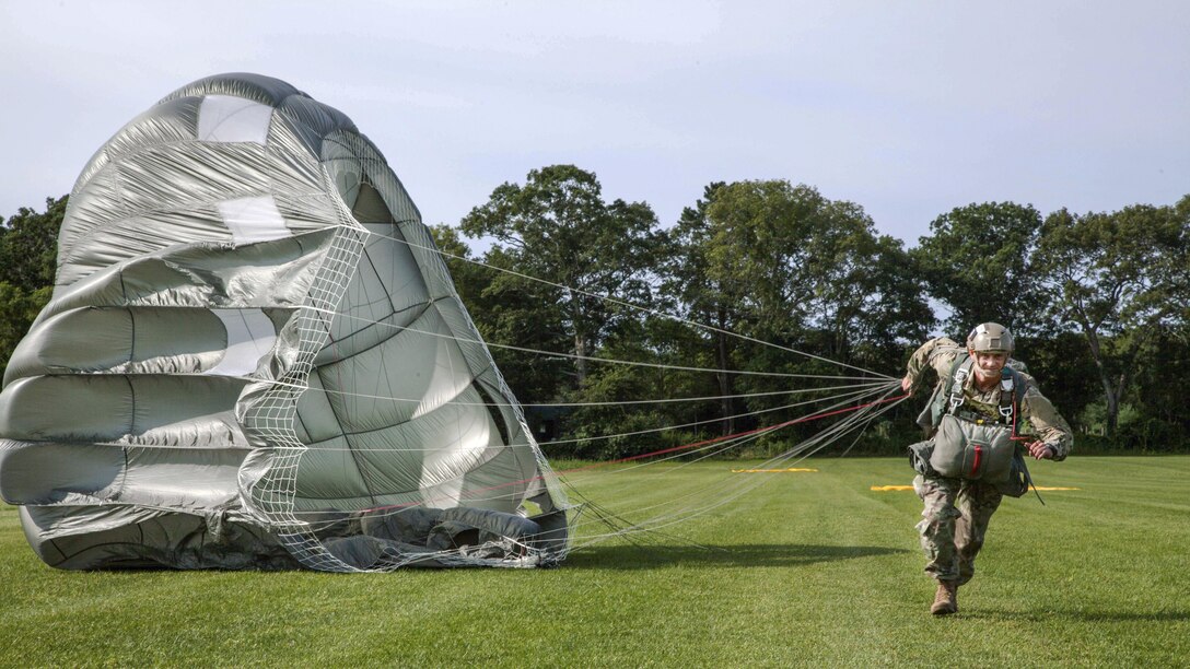 A paratrooper runs while holding the strings of his open parachute.