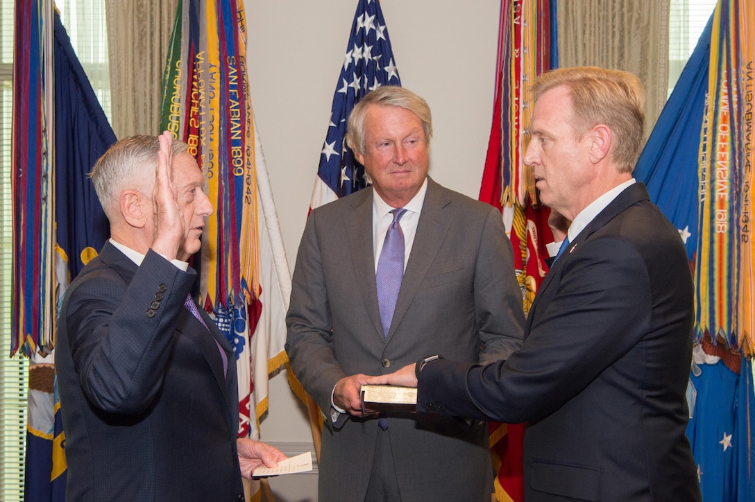 Defense Secretary Jim Mattis and Deputy Defense Secretary Pat Shanahan stand facing each other with right hands raised.