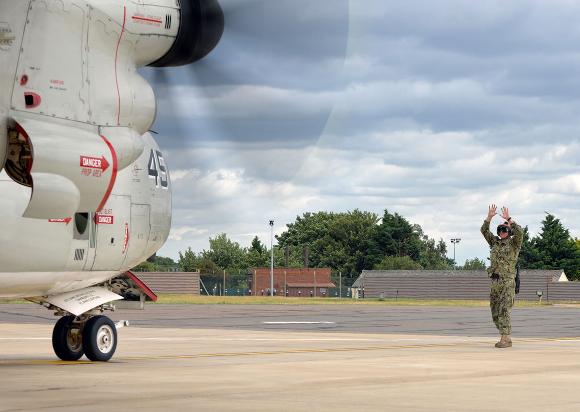 U.S. Navy Petty Officer 2nd Class Seth Neighbor, VRC-40 Naval aircrewman mechanical, gives marshalling signals to the pilots of a C-2A Greyhound on RAF Mildenhall, England, as they prepare to take off on a mission to the USS George H.W. Bush aircraft carrier (CVN77) Aug. 3, 2017. Two C-2A aircraft were TDY to RAF Mildenhall as part of Exercise Saxon Warrior, a multinational joint maritime exercise involving 15 warships from five different nations, along with submarines, more than 100 aircraft and approximately 9,000 personnel. (U.S. Air Force photo by Karen Abeyasekere)