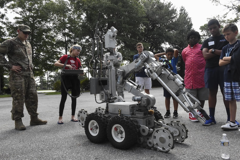 Staff Sgt. Sherwood Johnson, 628th Civil Engineer Squadron explosive ordnance disposal apprentice, watches Sara Welch, a Science, Technology, Engineering and Mathematics Day participant, operate one of the EOD F6B bomb disposal robots attempting to pick up a bottle of water at the Chapel Annex in Joint Base Charleston, S.C., Aug. 14.