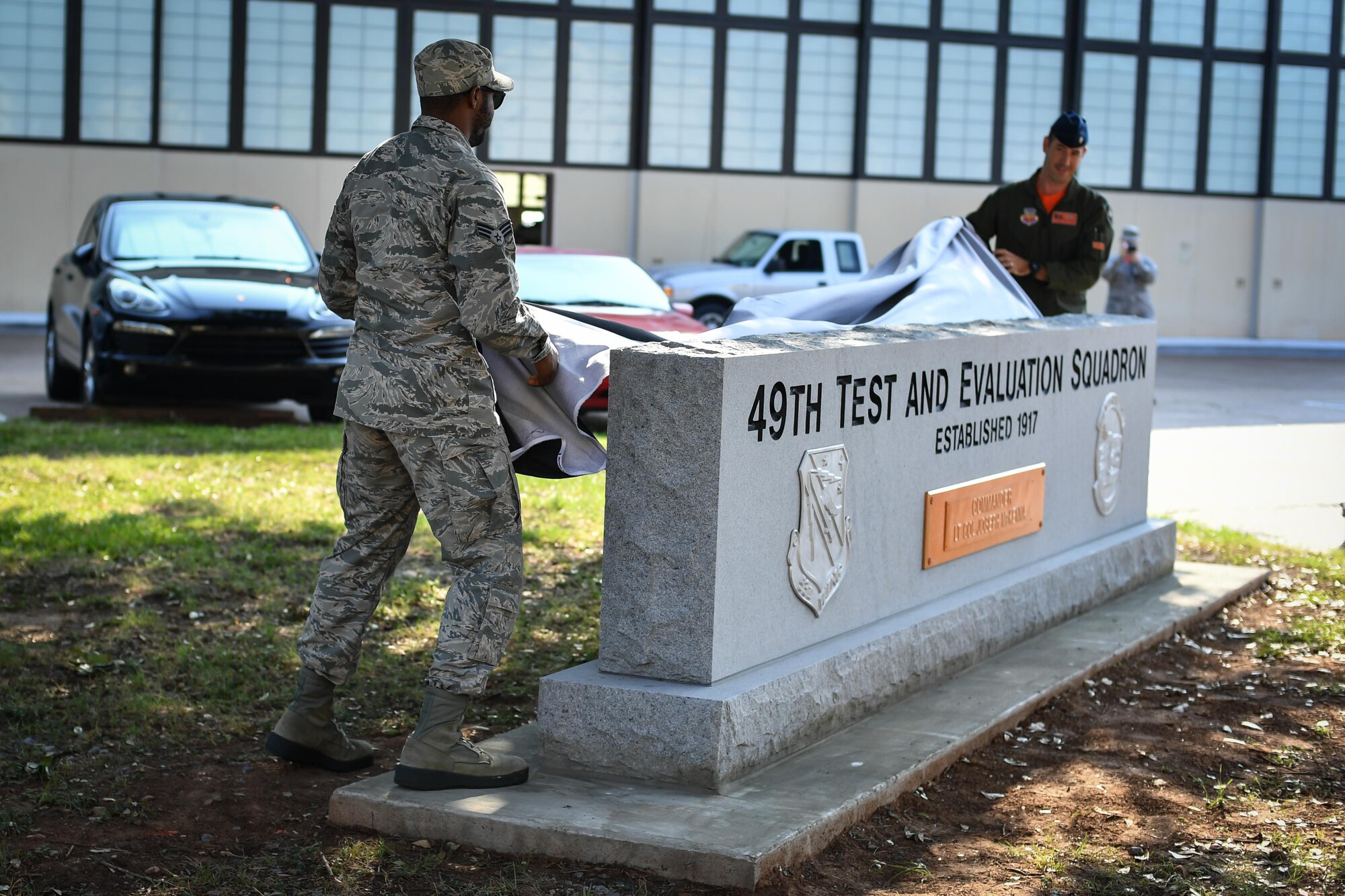 Senior Airman Donald Harris, 49th Test and Evaluation Squadron aviation resource management (left) and Lt. Col. Joseph McKenna, 49th Test and Evaluation Squadron commander (right) unveil a monument during the squadron’s centennial celebration at Barksdale Air Force Base, La., Aug. 2, 2017. As the youngest member of the squadron, Harris was chosen by the commander to assist with the unveiling of the monument. (U.S. Air Force Photo/Senior Airmen Mozer O. Da Cunha)