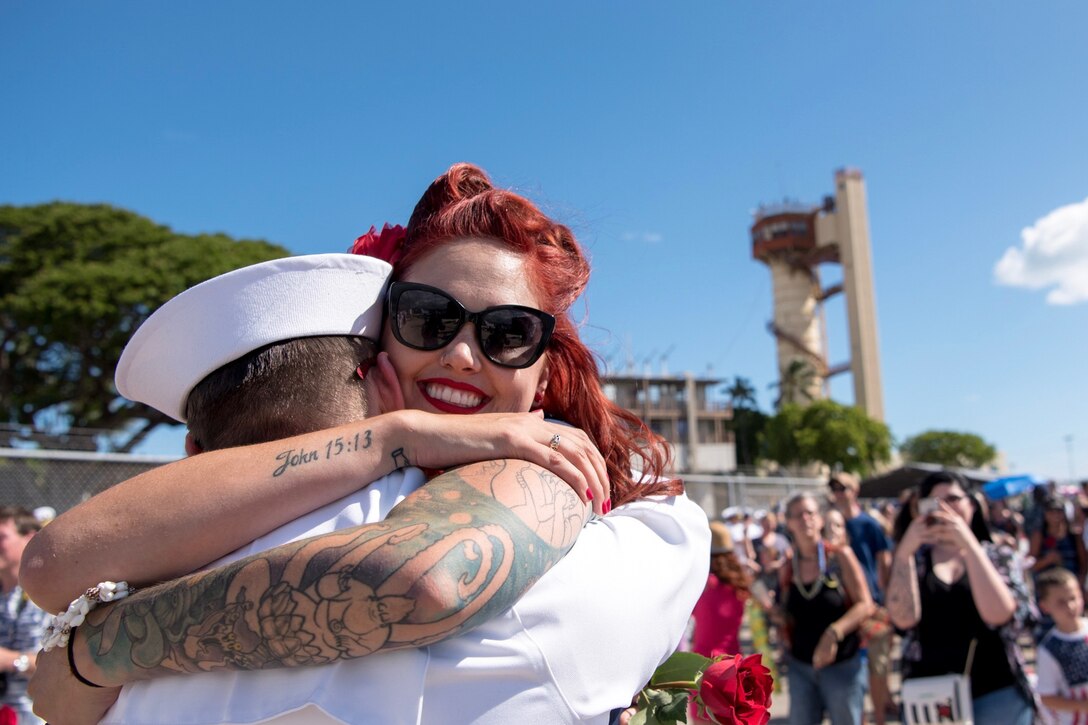 A woman hugs a sailor as a crowd of people lingers in the background.