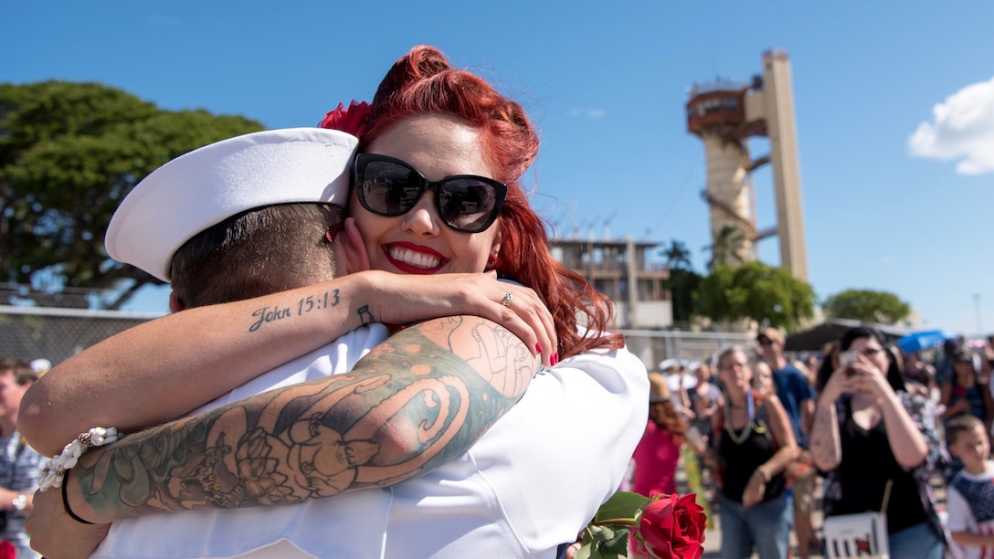 A woman hugs a sailor as a crowd of people lingers in the background.