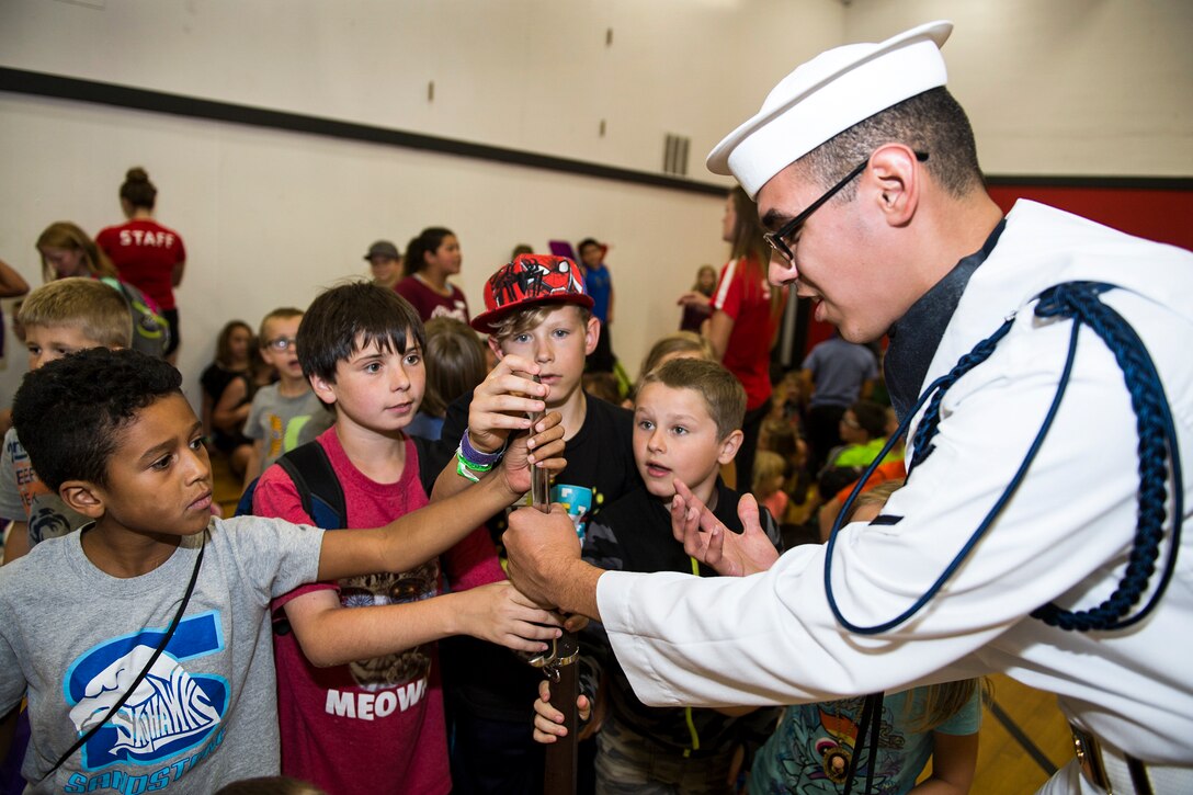 A sailor holds a weapon as children touch it during a Navy Week event.