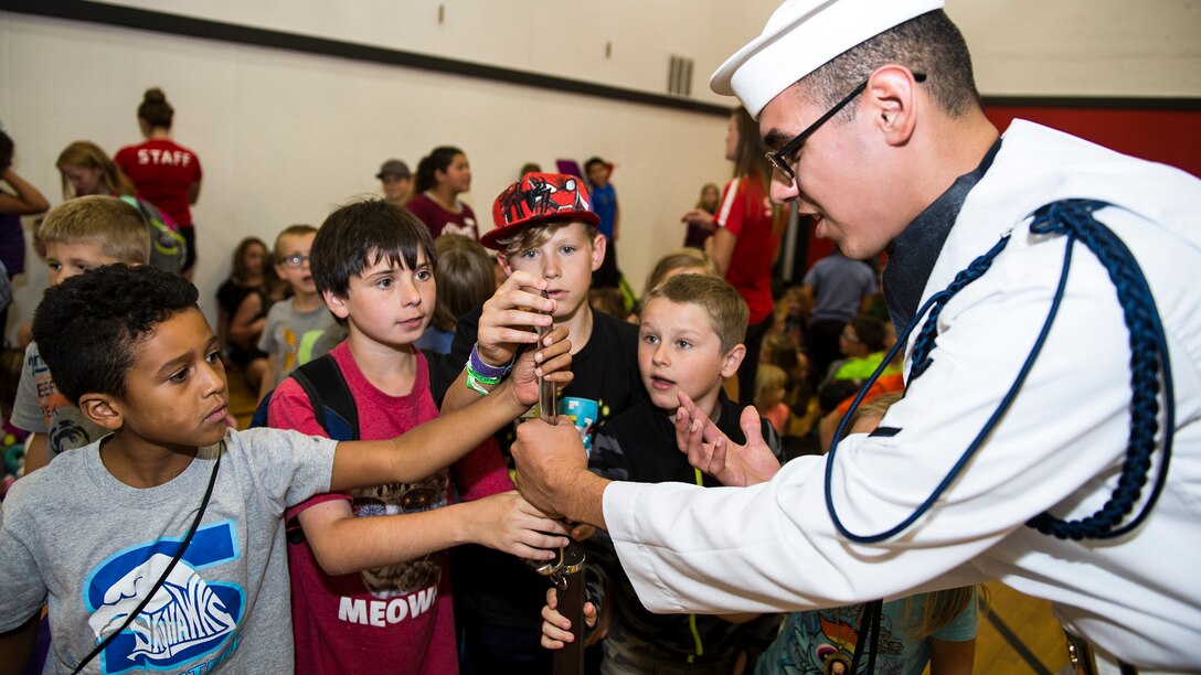 A sailor holds a weapon as children touch it during a Navy Week event.