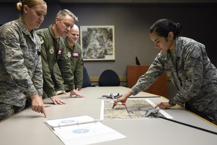 Service members stand at a table to get a briefing.