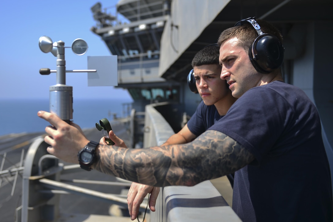 Navy Petty Officer 3rd Class Christopher Clark, right, trains Seaman Dylan Eaton on how to use a handheld anemometer.