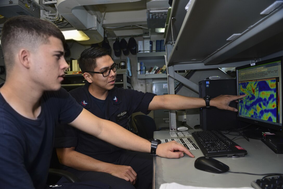 Navy Petty Officer 2nd Class Erwin Begay, left, trains Seaman Dylan Eaton on how to read high level wind reports.
