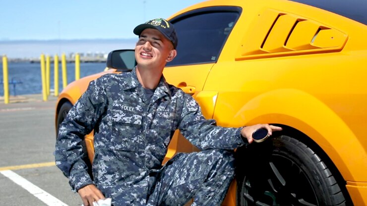 This image shows a sailor smiling as he pauses while polishing a yellow car.