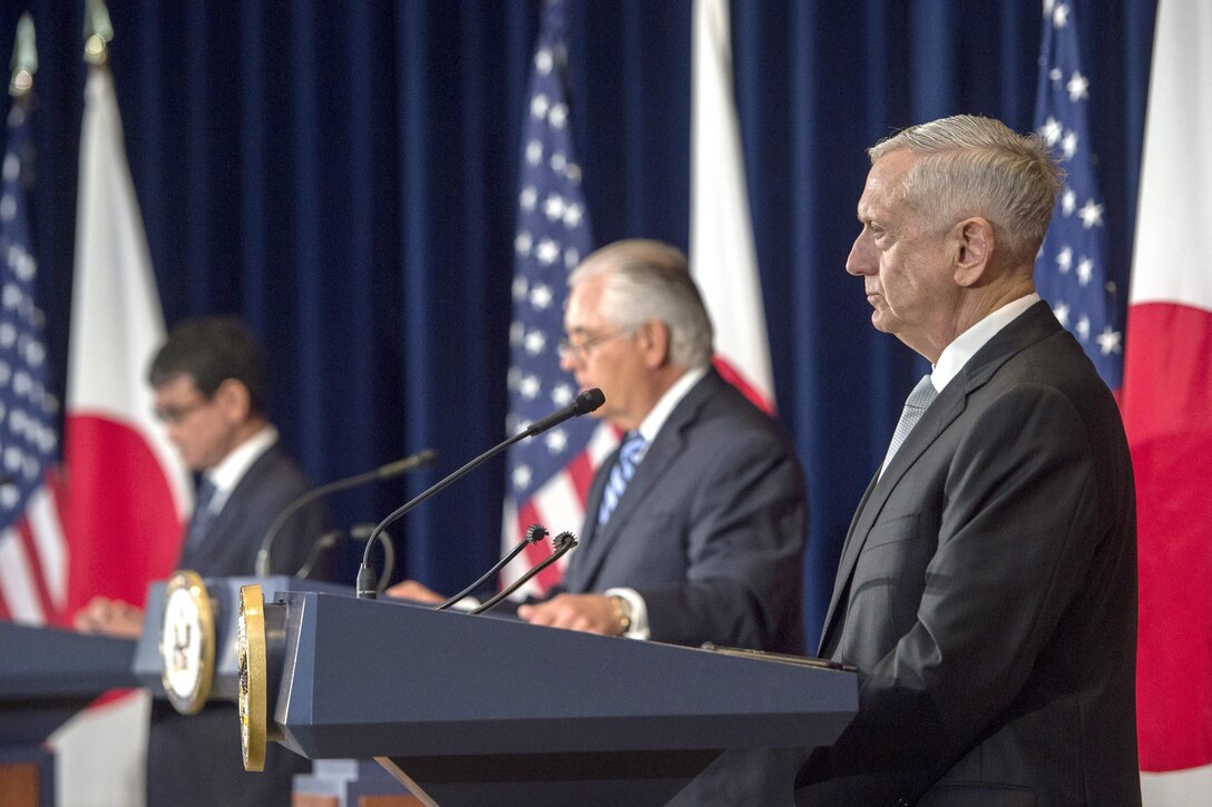 Defense Secretary Jim Mattis listens while on stage two other people.