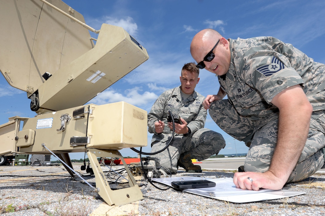 Two airmen work outside on communications equipment.