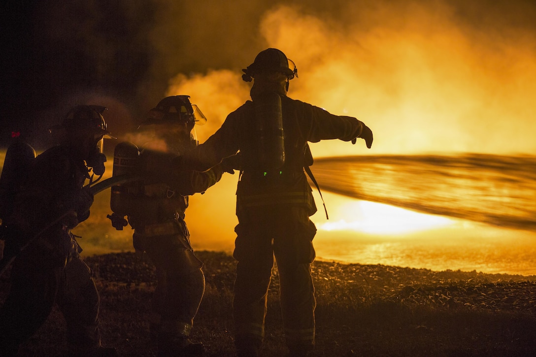 Soldiers train at night to extinguish yellow flames using a hose and water.