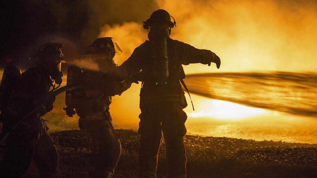 Soldiers train at night to extinguish yellow flames using a hose and water.