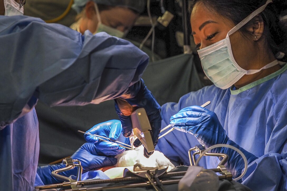 Airmen in blue gowns and masks train during a simulated surgery as part of an exercise.