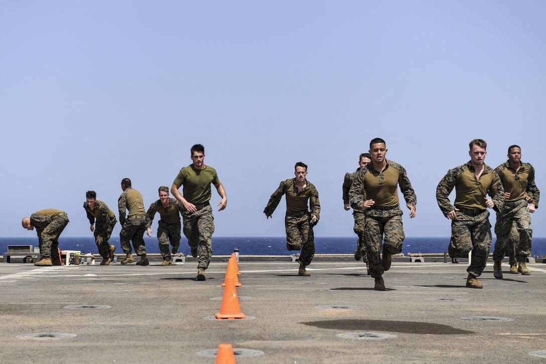 Marines sprint during physical training on a a ship's flight deck.
