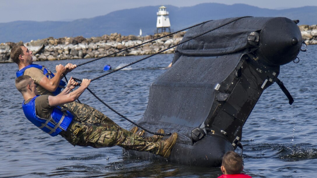Soldiers try to right a zodiac boat during capsizing training in the water.