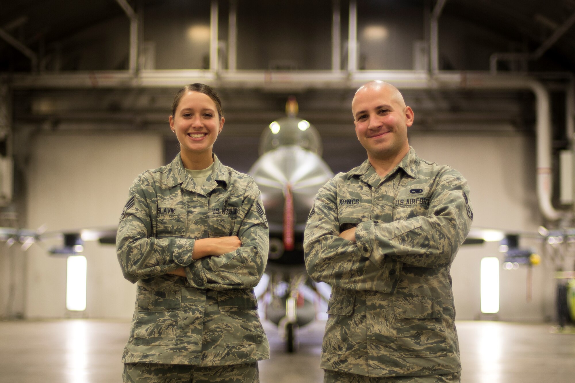 U.S. Air Force Senior Airman Amber Slavik, left, a 35th Medical Support Squadron medical logistics technician, and Airman 1st Class Anthony Kovacs, Jr., right, a 14th Fighter Squadron crew chief, pose in front of an F-16 Fighting Falcon at Misawa Air Base, Japan.