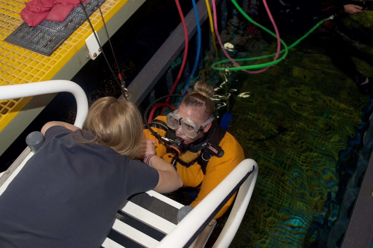 Instructor helping soldier out of shark tank.