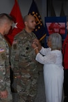 Left to Right: U.S. Army Col. Brad J. Eungard, commander of Defense Logistics Agency (DLA)  Distribution Susquehanna, Pennsylvania., watches as U.S. Army 1st Sgt. Maximo Nunez receives his promotion from his grandmother, Carmen Julia Peralta, before assuming responsibility as DLA Distribution, Susquehanna, Pa. Installation Senior Enlisted Advisor and 1st Sgt. during a ceremony held August 15, 2017 at the DLA Distribution Center, Susquehanna, Pa.