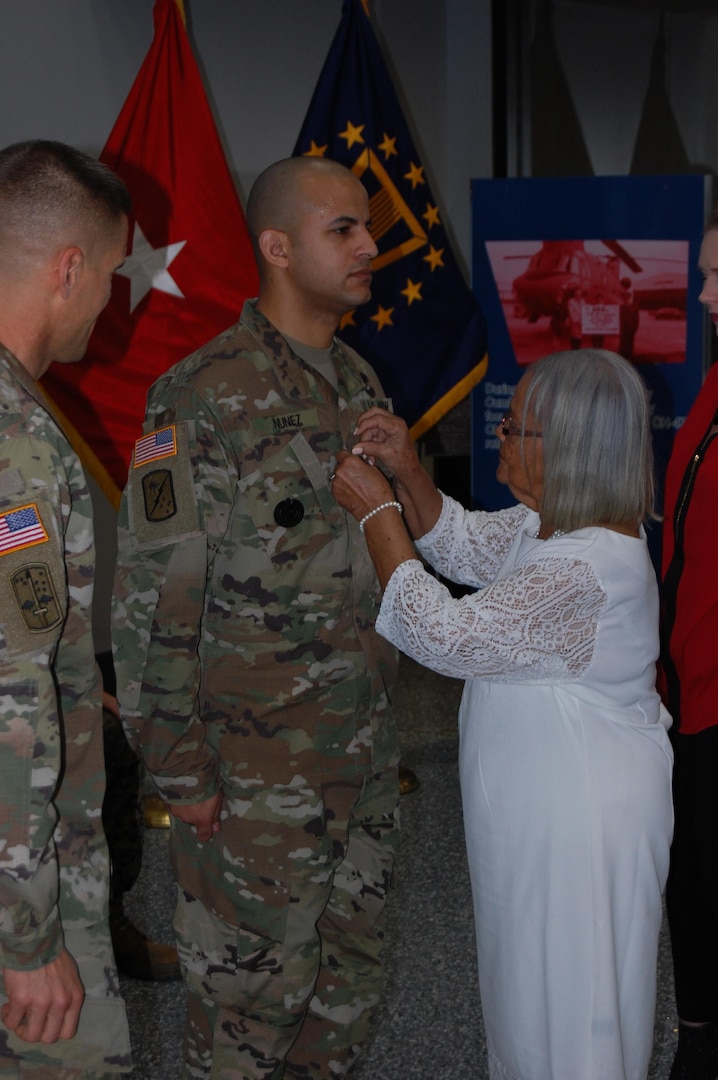 Left to Right: U.S. Army Col. Brad J. Eungard, commander of Defense Logistics Agency (DLA)  Distribution Susquehanna, Pennsylvania., watches as U.S. Army 1st Sgt. Maximo Nunez receives his promotion from his grandmother, Carmen Julia Peralta, before assuming responsibility as DLA Distribution, Susquehanna, Pa. Installation Senior Enlisted Advisor and 1st Sgt. during a ceremony held August 15, 2017 at the DLA Distribution Center, Susquehanna, Pa.