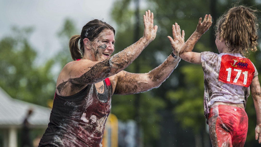 A mud-covered woman and girl clap hands during a mud run.