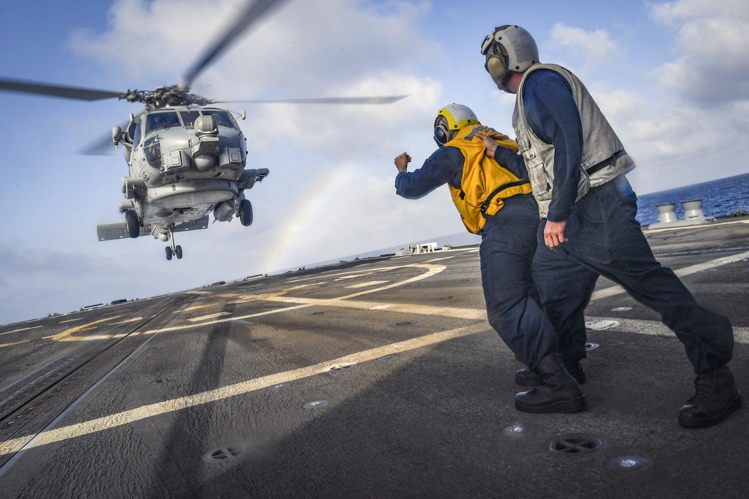 Sailors stand on a ship's flight deck as a helicopter comes in for a landing.
