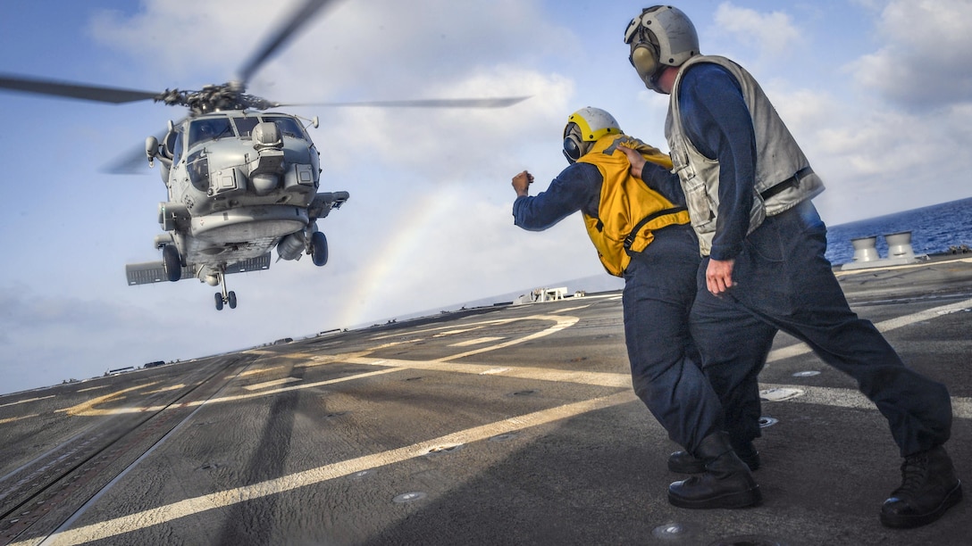Sailors stand on a ship's flight deck as a helicopter comes in for a landing.