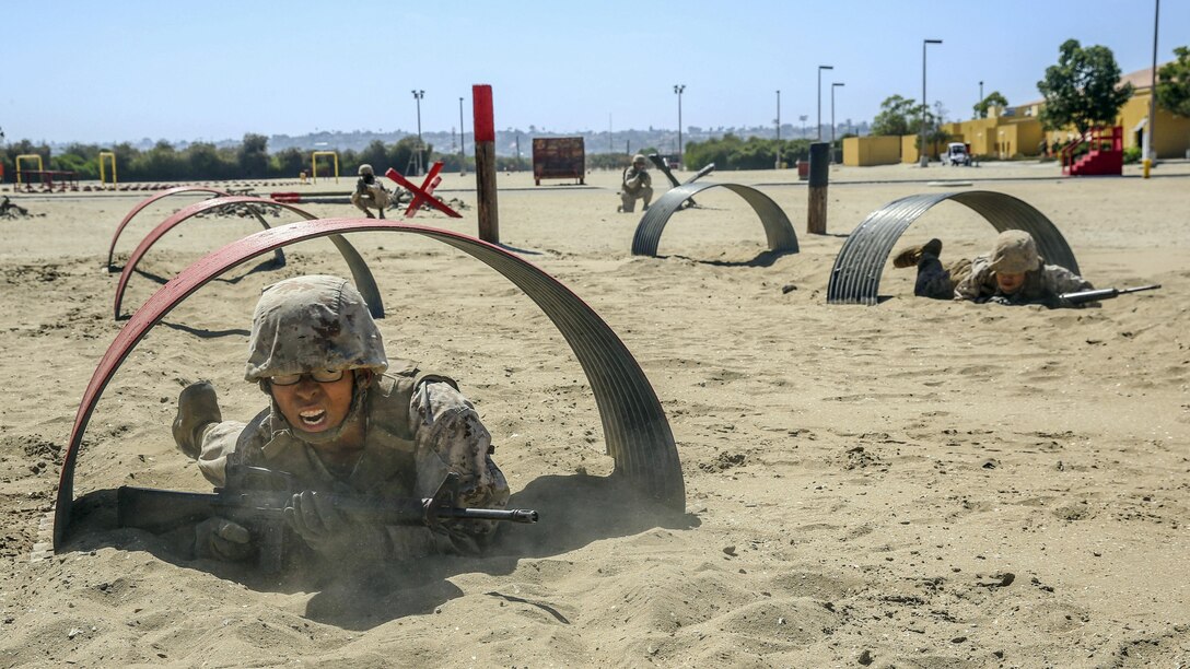 Marines low-crawl through tunnels in the sand.