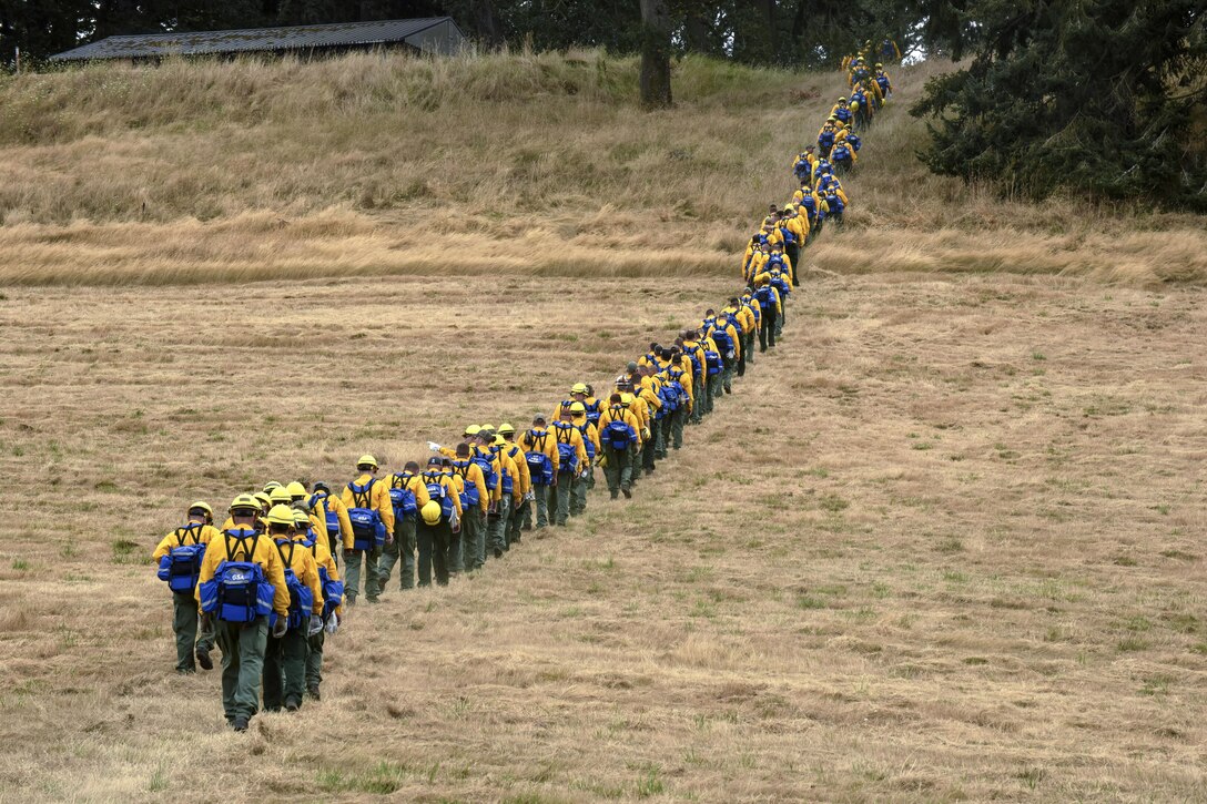 A long line of service members hike up dry, grassy terrain.