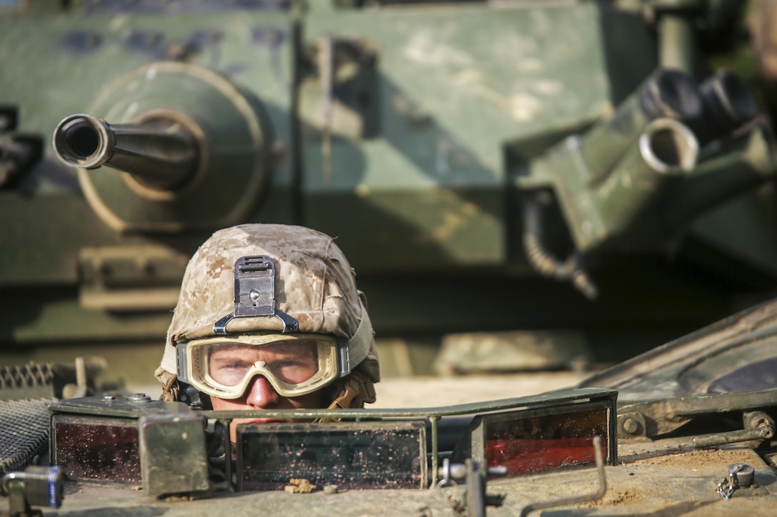 A helmet- and goggles-clad Marine's eyes and nose are visible as he looks out the top opening of a tactical vehicle.