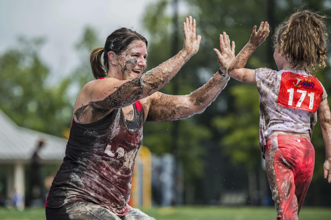 A mud-covered woman and girl clap hands during a mud run.