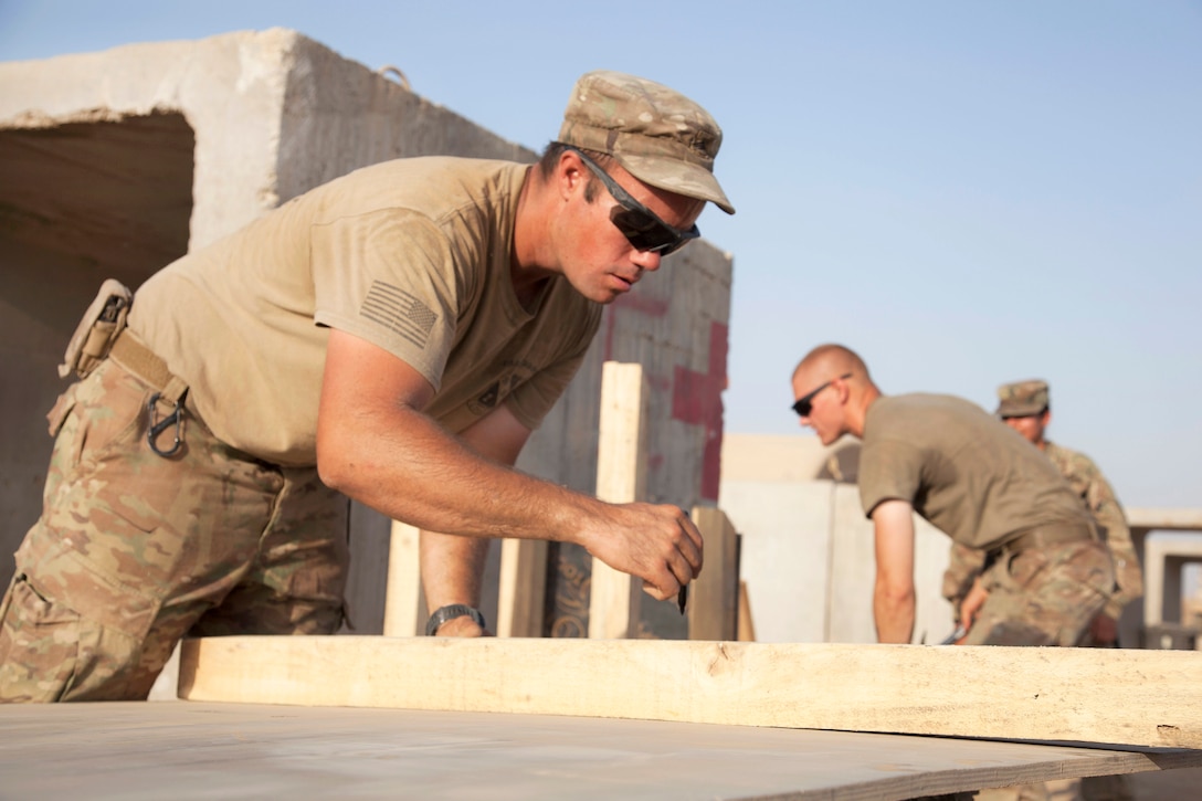 A soldier marks a board before cutting while building a podium.