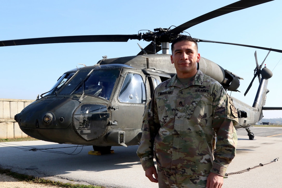 Staff Sgt. Oscar Morales stands in front of a helicopter.