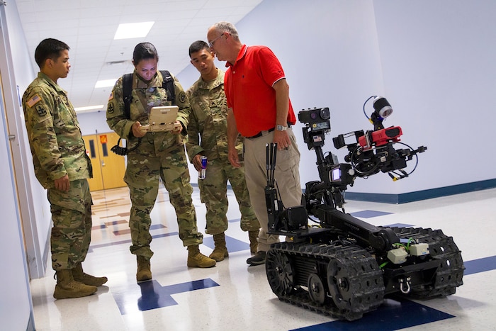 Soldiers look at a computer tablet screen while standing next to an unmanned robot.