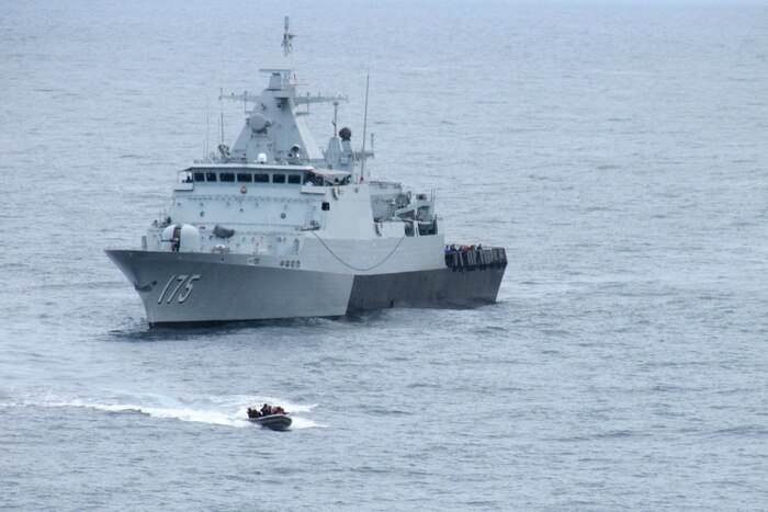 A small water vehicle approaches a large ship in the ocean.