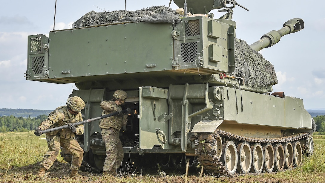 Soldiers use a metal bar to push into an opening in the back of a tactical vehicle.