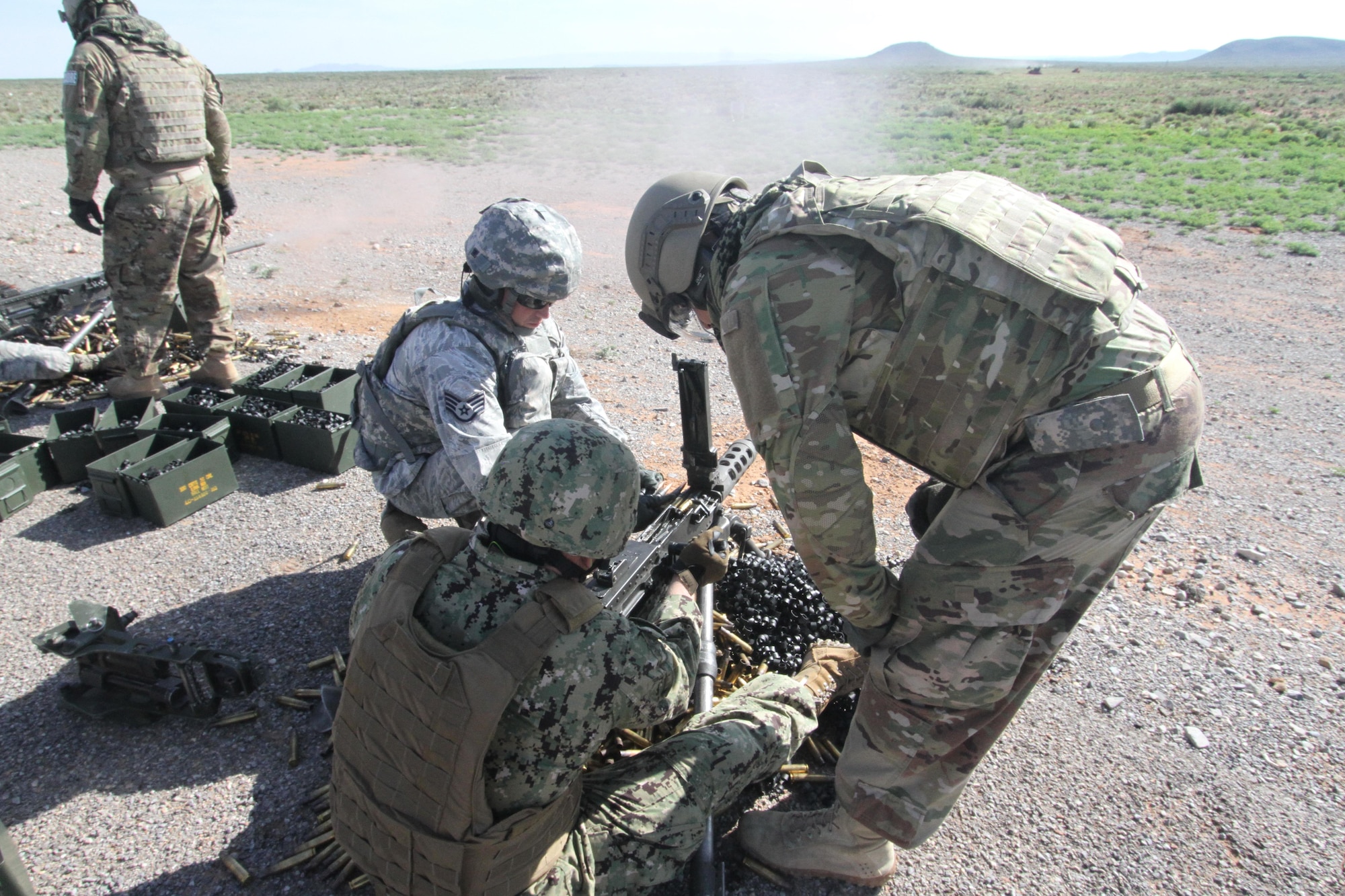 Gunner U.S. Petty Officer 3rd Class Derek Dick waits to charge an M2 .50 caliber machine gun while assistant gunner Staff Sgt. Joshua Hopkins loads ammunition during heavy weapons firing on Fort Bliss' Range 39 July 26, 2017, as cadre member Tech. Sgt. Jose Marrero looks on.