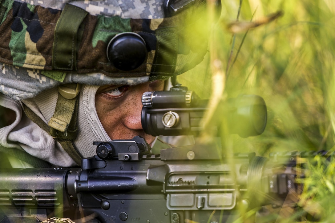 An airman looks down the scope of a rifle during an outdoor exercise.