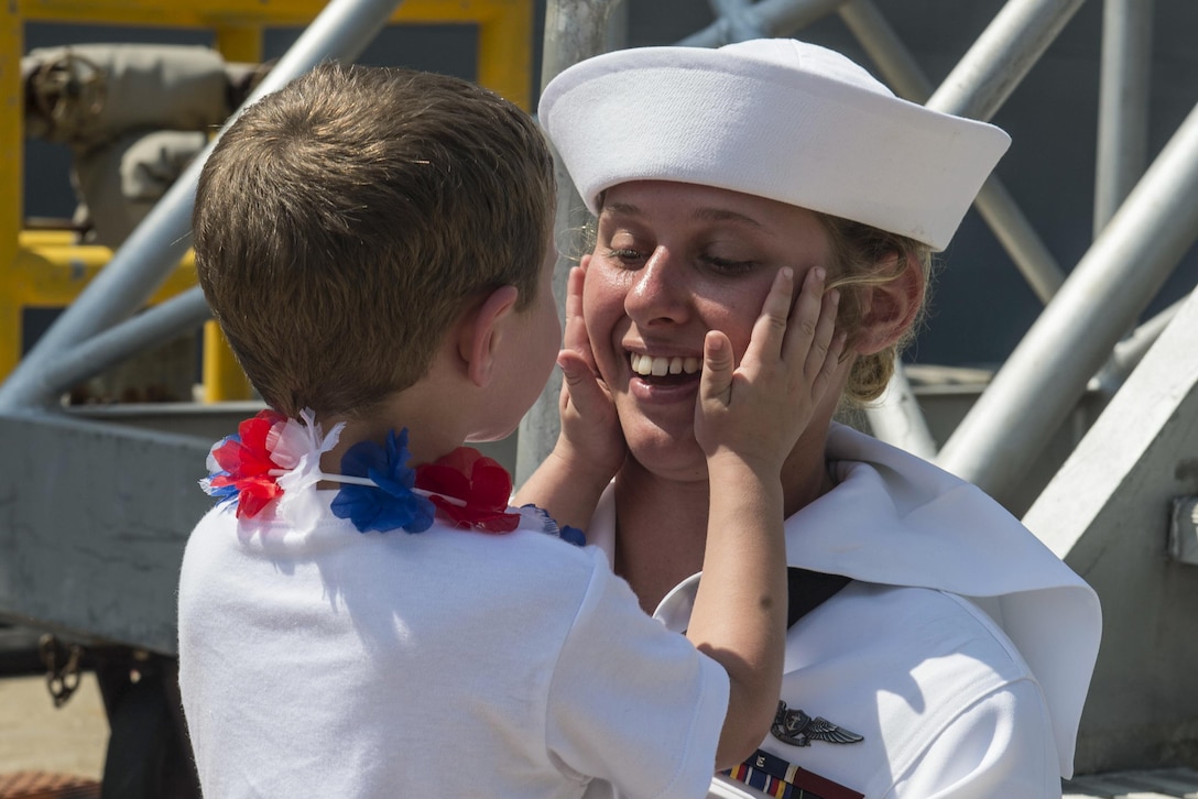 A sailor greets a young family member after departing a ship.
