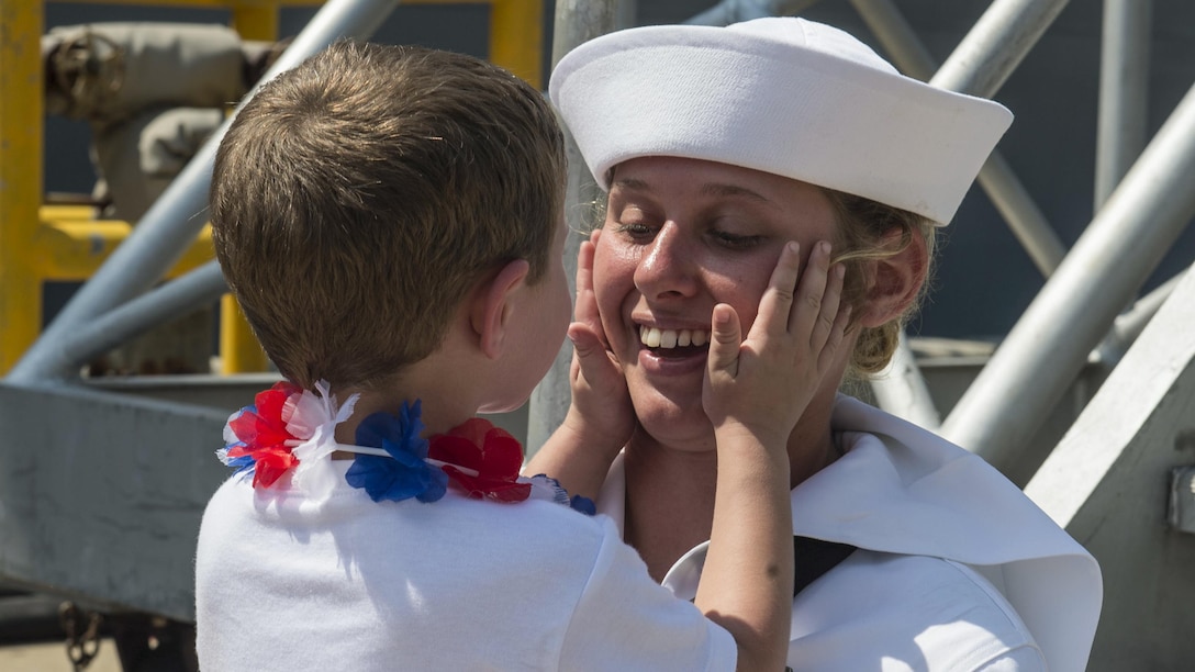 A sailor greets a young family member after departing a ship.