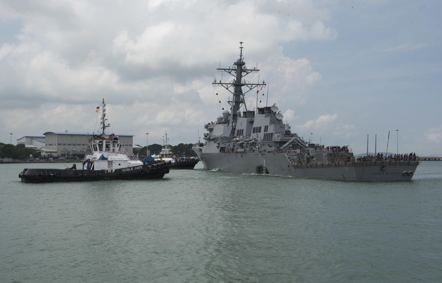 CHANGI NAVAL BASE, REPUBLIC OF SINGAPORE (Aug. 21, 2017) Tugboats from Singapore assist the guided-missile destroyer USS John S. McCain (DDG 56) as it steers towards Changi Naval Base, Republic of Singapore following a collision with the merchant vessel Alnic MC while underway east of the Straits of Malacca and Singapore on Aug. 21. Significant damage to the hull resulted in flooding to nearby compartments, including crew berthing, machinery, and communications rooms. Damage control efforts by the crew halted further flooding. The incident will be investigated. (U.S. Navy photo by Mass Communication Specialist 2nd Class Joshua Fulton/Released)