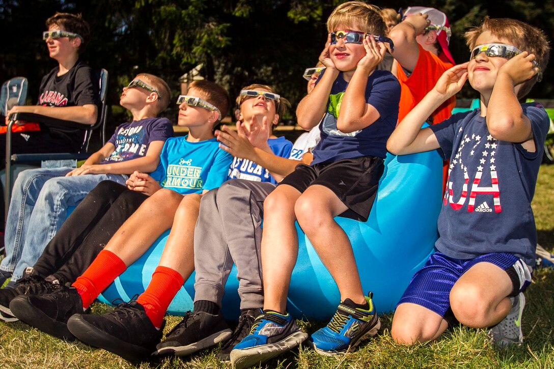 Children sit together with eclipse glasses looking up.