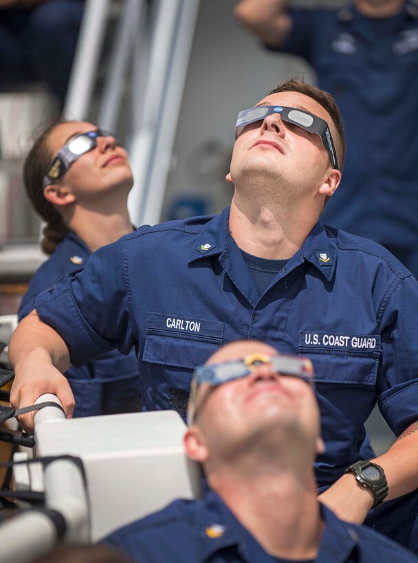 Coast Guard crew members look up wearing glasses to watch the solar eclipse.
