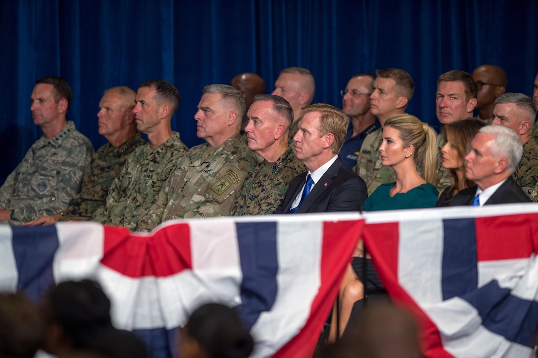 American military and political officials sit in while listening to a speech.