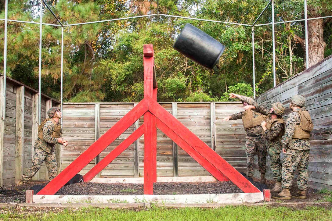 Marines toss a plastic barrel over an obstacle.