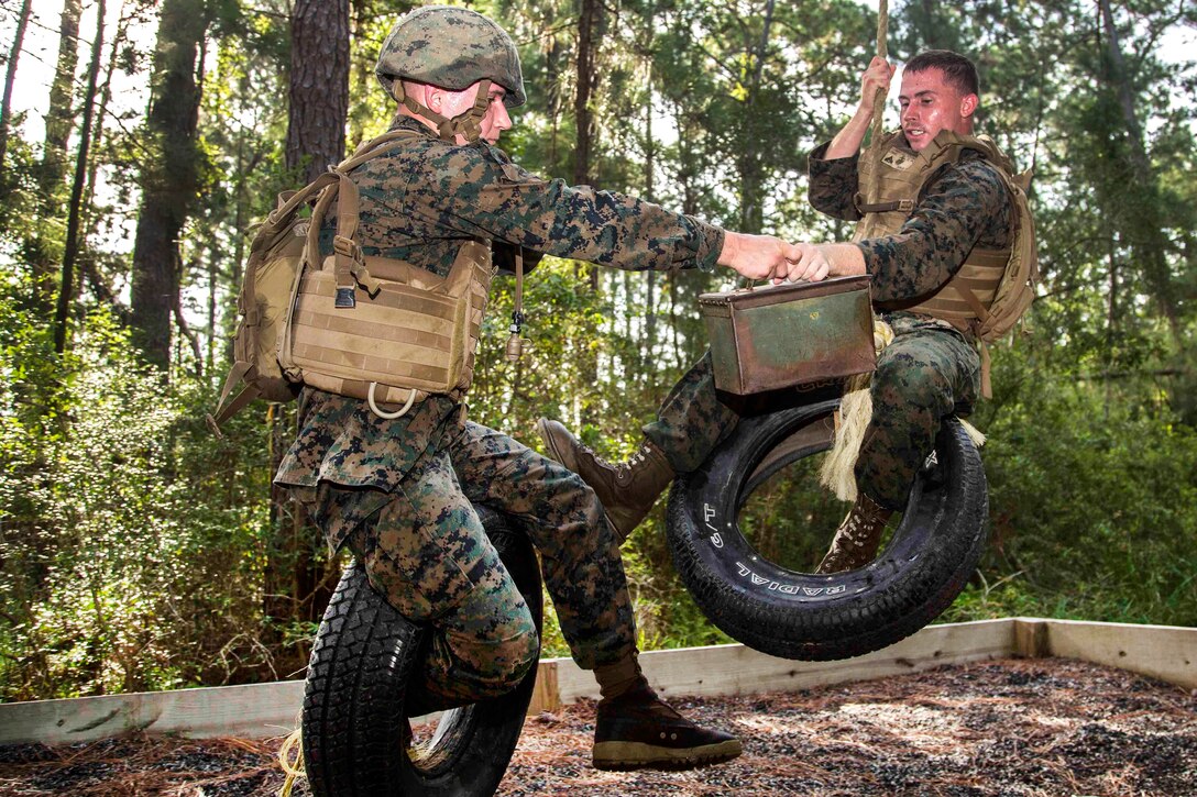 Marines swing on ropes and tires transferring a ammo can.