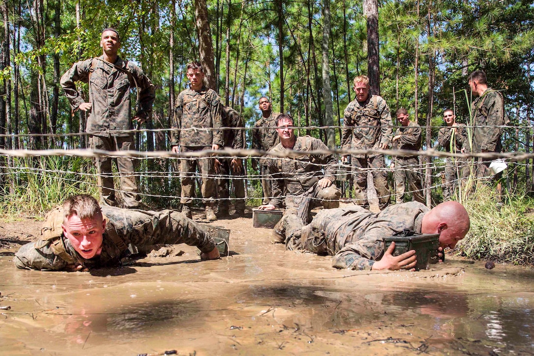 Marines crawl under barbed wire through the mud pit.